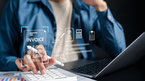 © iStockphoto/champpixs Employee using laptop and calculator with digital symbols for e-invoicing, automated invoice processing and tax documents.