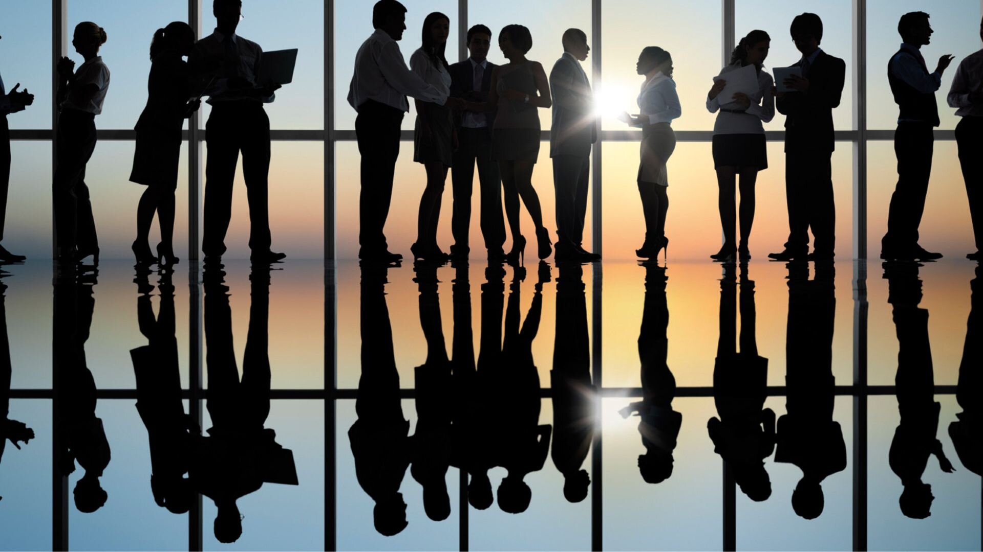 Silhouettes of businesspeople standing and talking in a modern office with large windows during sunset, reflecting teamwork and networking